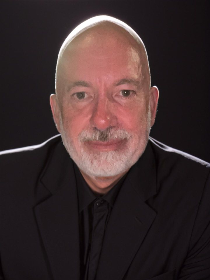 Portrait of author Spencer Bridge, photographed against a black background in a dark jacket.